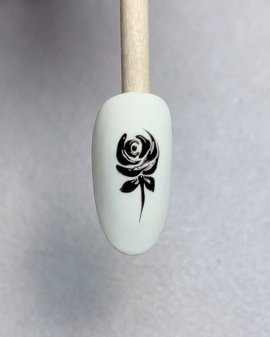 A close-up of a fine liner brush painting small pointed leaves onto a black stem on a nail.