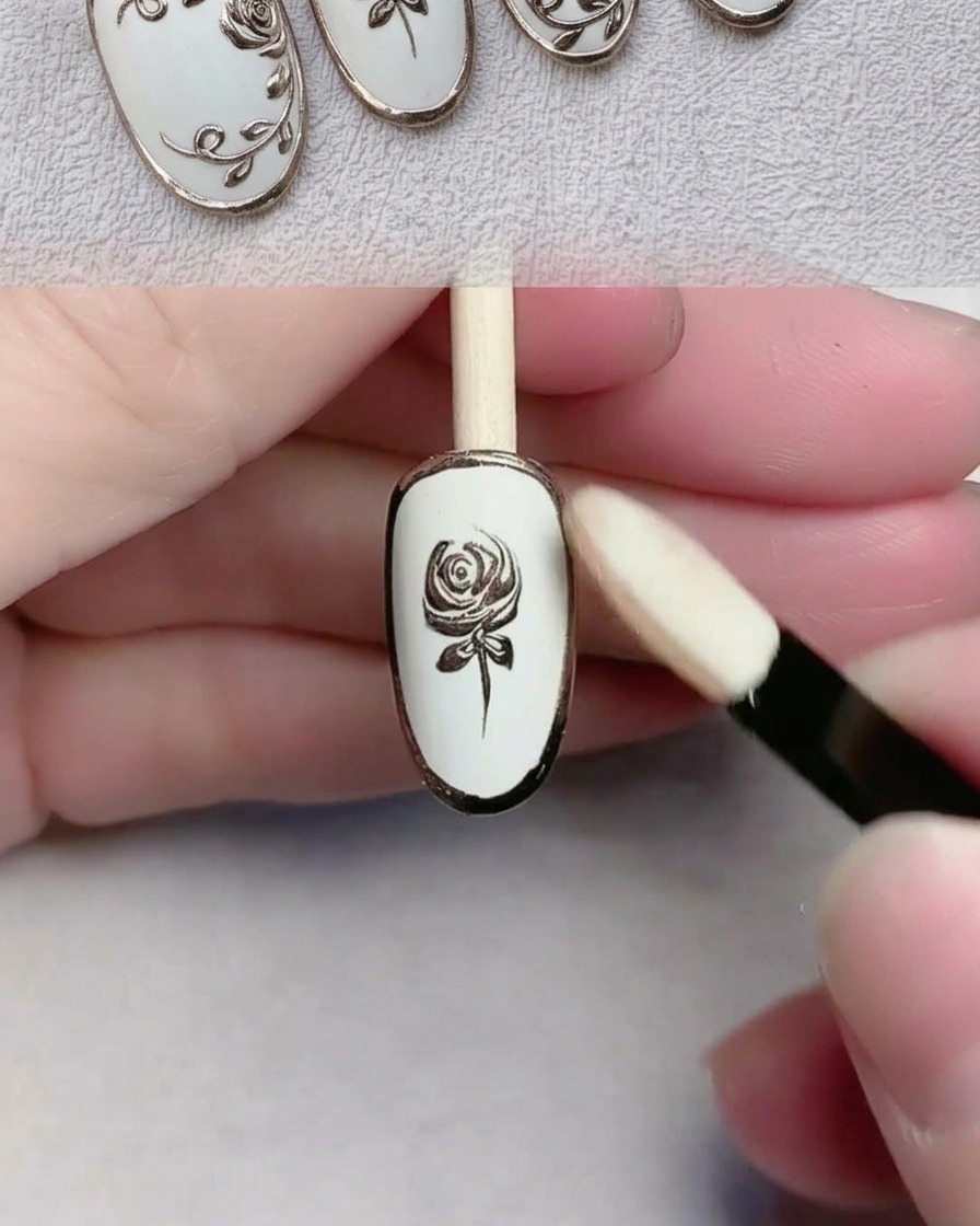 An eyeshadow sponge applicator buffing gold chrome powder onto a detailed nail design.