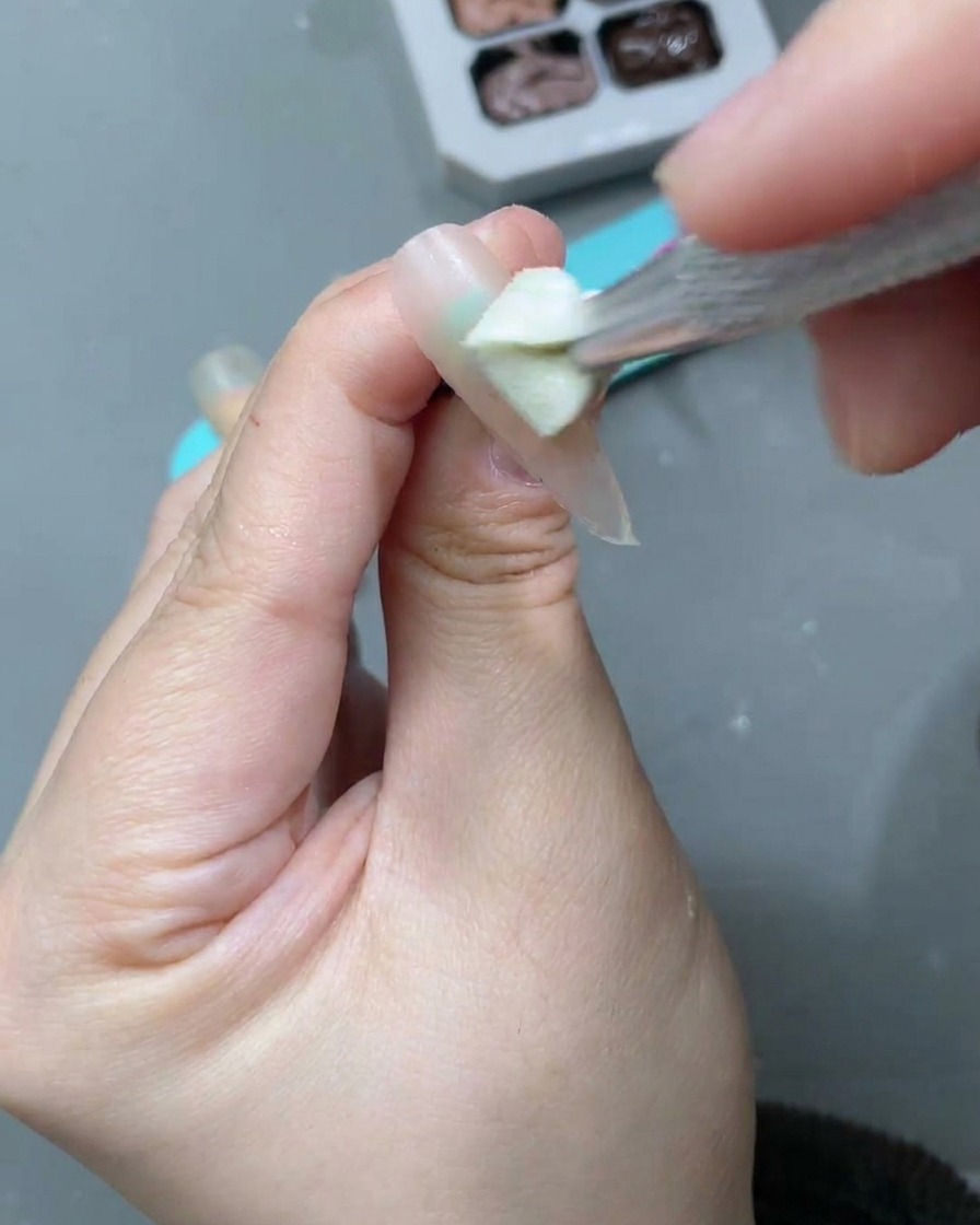 A nail brush applying a white moon cat-eye gel over the previously applied nude base.