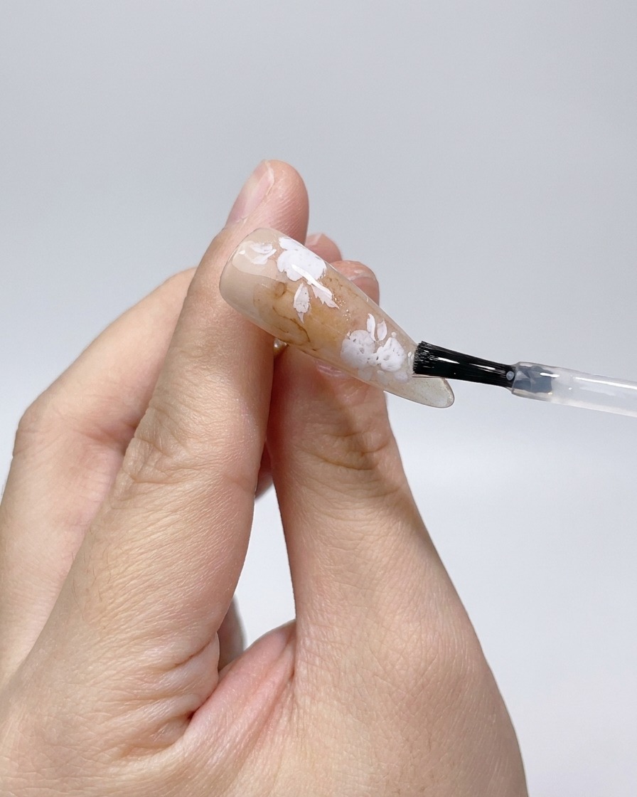 Applying a matte top coat over the white rose outlines on the nail.