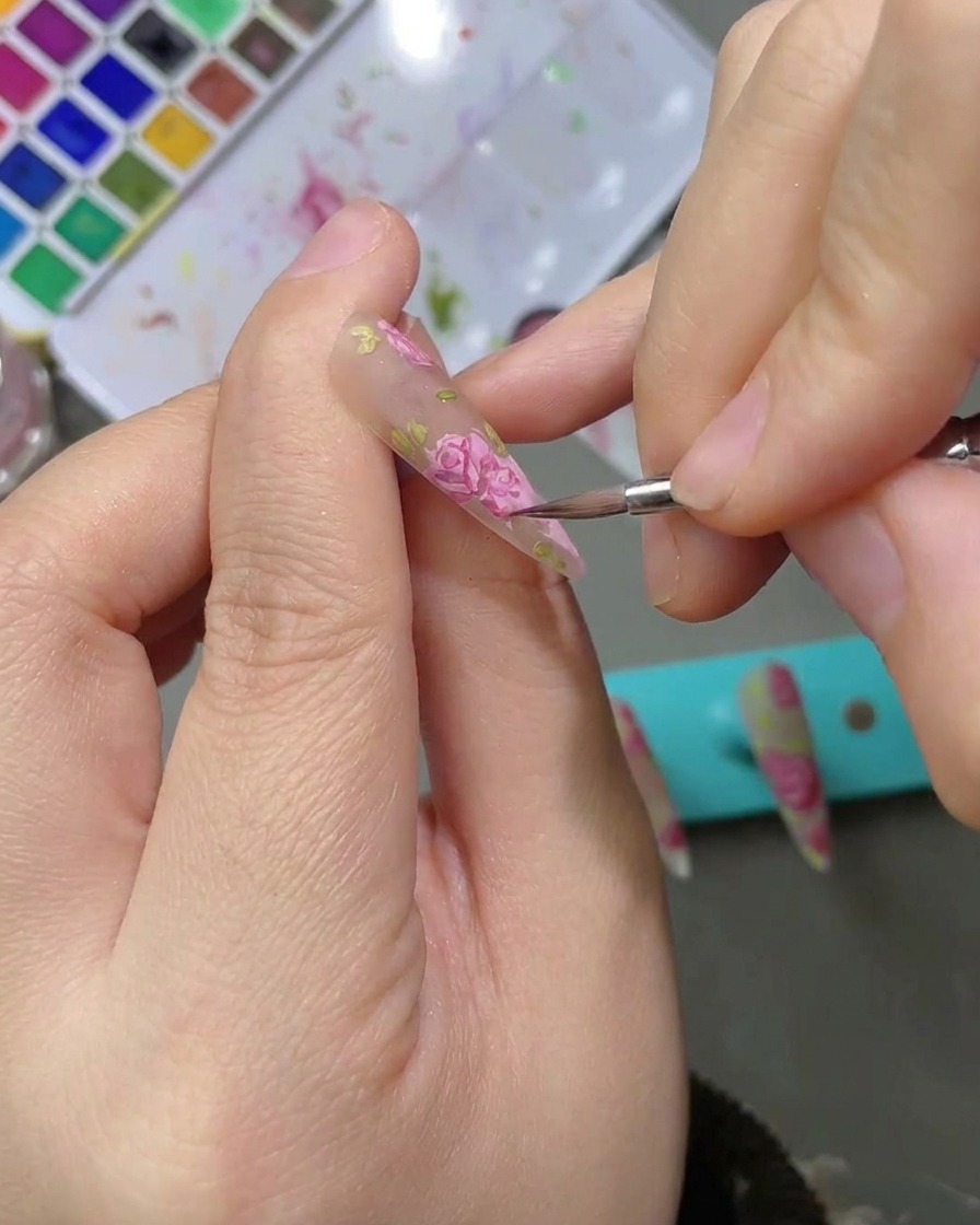 The application of a matte top coat over a finished, detailed watercolor rose nail design.