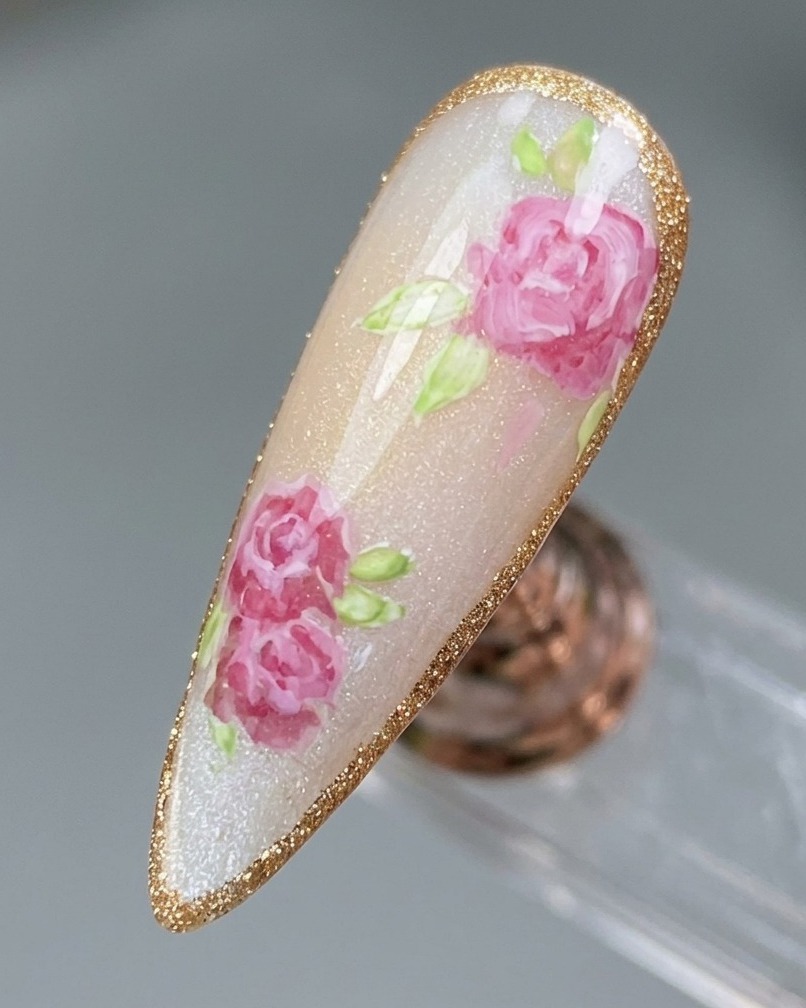 A close-up of a finished rose nail design being traced with a delicate, shimmering platinum gel border.