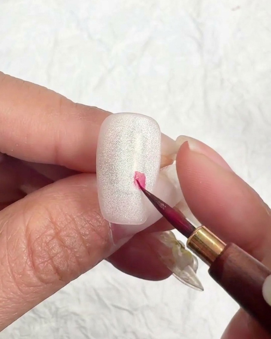 A fine liner brush placing a small pink dot on the nail to begin a cherry blossom.