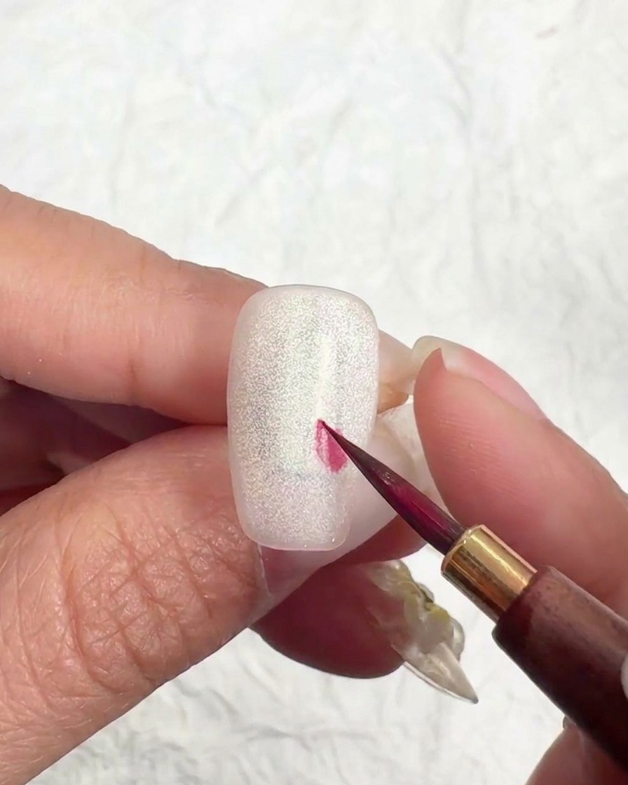 A liner brush pulling color outward from a center point to form a petal shape.