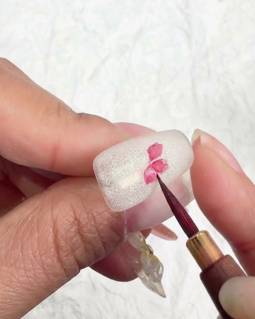 A close-up of a cherry blossom design on a nail, with lighter pink pigment being added to the tips of the petals.