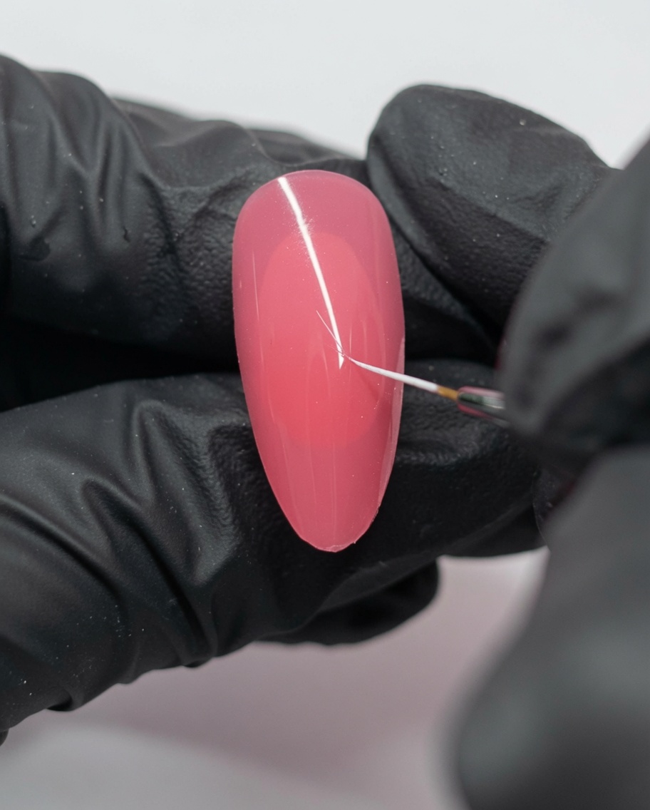 A close-up of a pink nail with a small white dot and a thin line drawn by a liner brush.