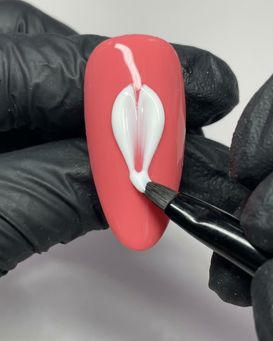 A nail art brush applying white gel to form the left side of a petal on a pink nail.