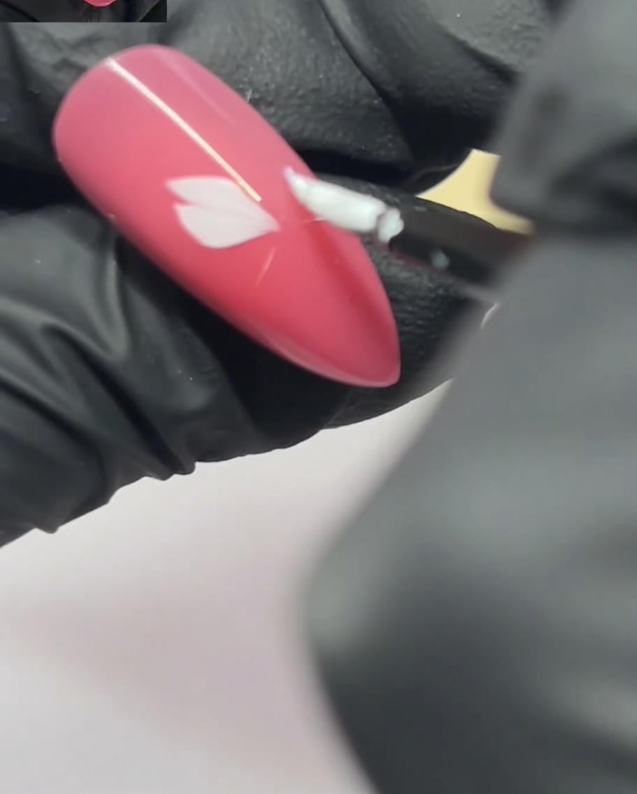A nail art brush applying a second petal next to the first one on a pink nail.