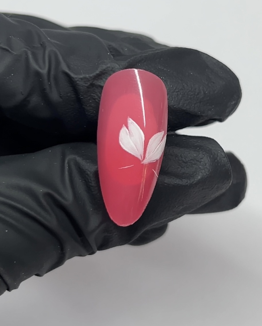 A close-up of a nail showing three white petals of a cherry blossom design against a pink base.