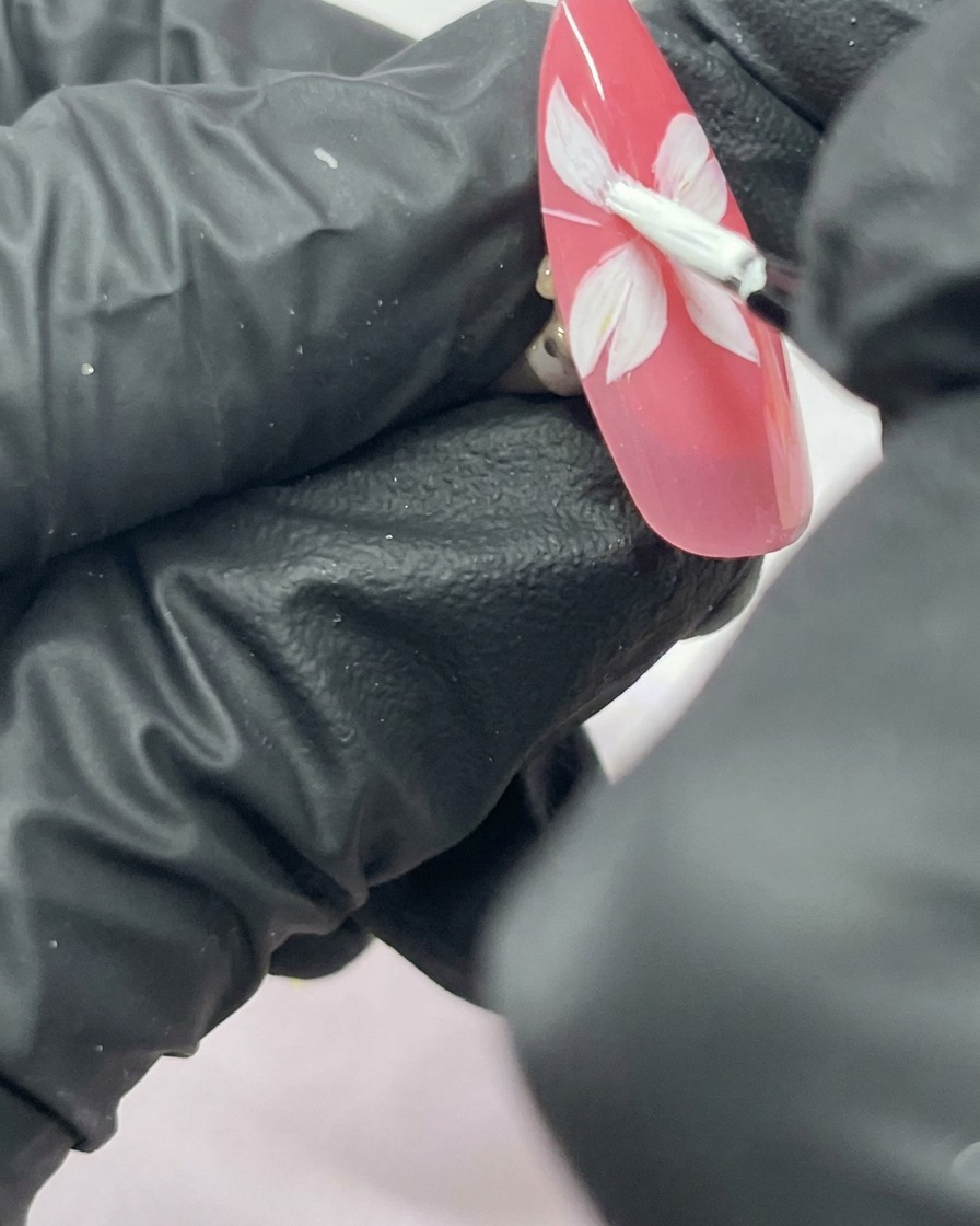 A close-up of a nail with a five-petaled white cherry blossom flower painted on a pink background.