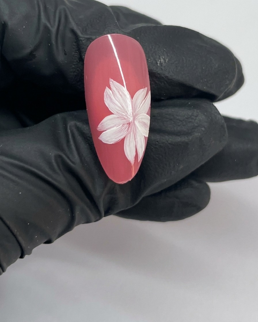 A close-up of a finished cherry blossom nail art design featuring a completed flower with a white stamen center.