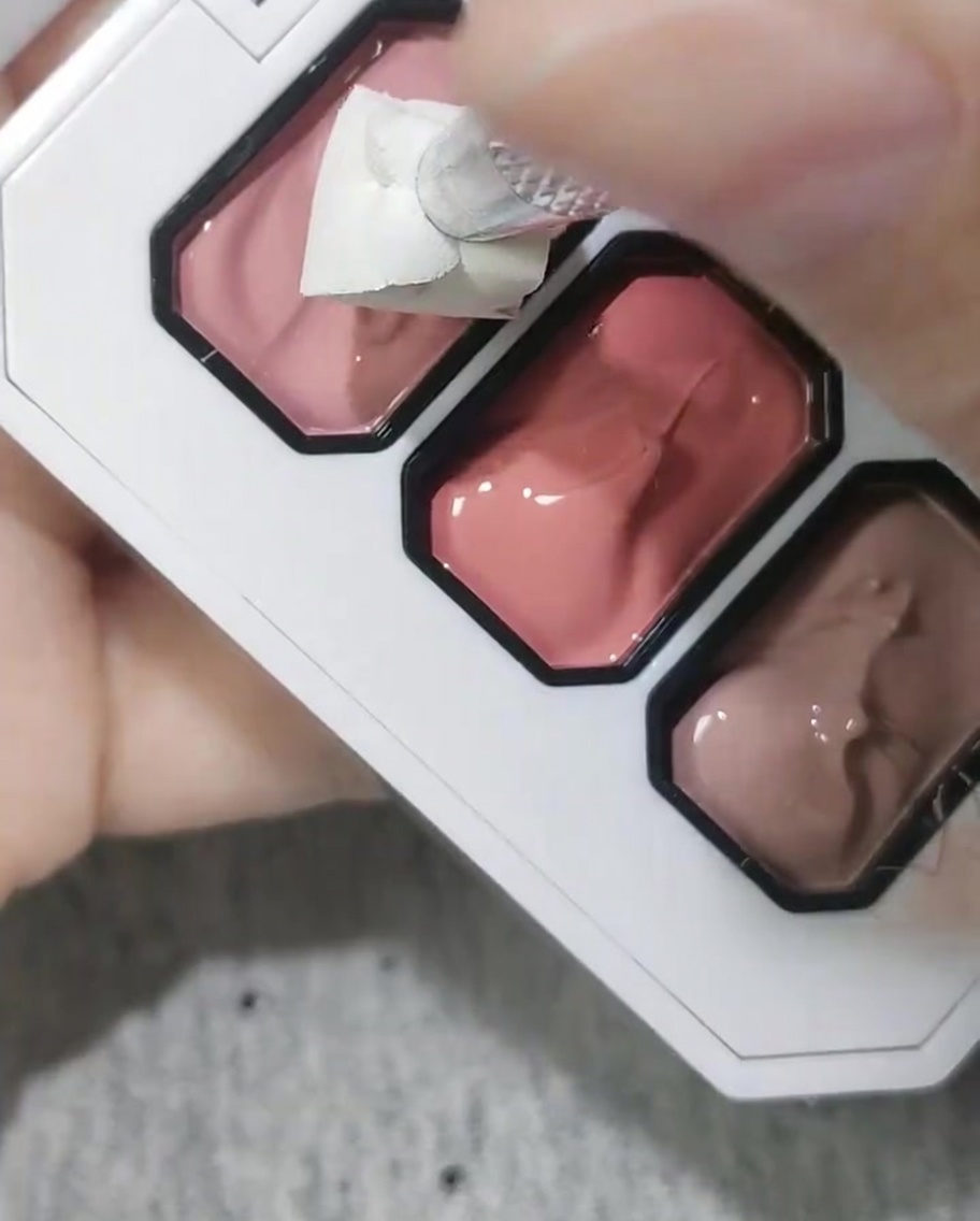 A cosmetic sponge being used to dab pink gel onto a nail tip.