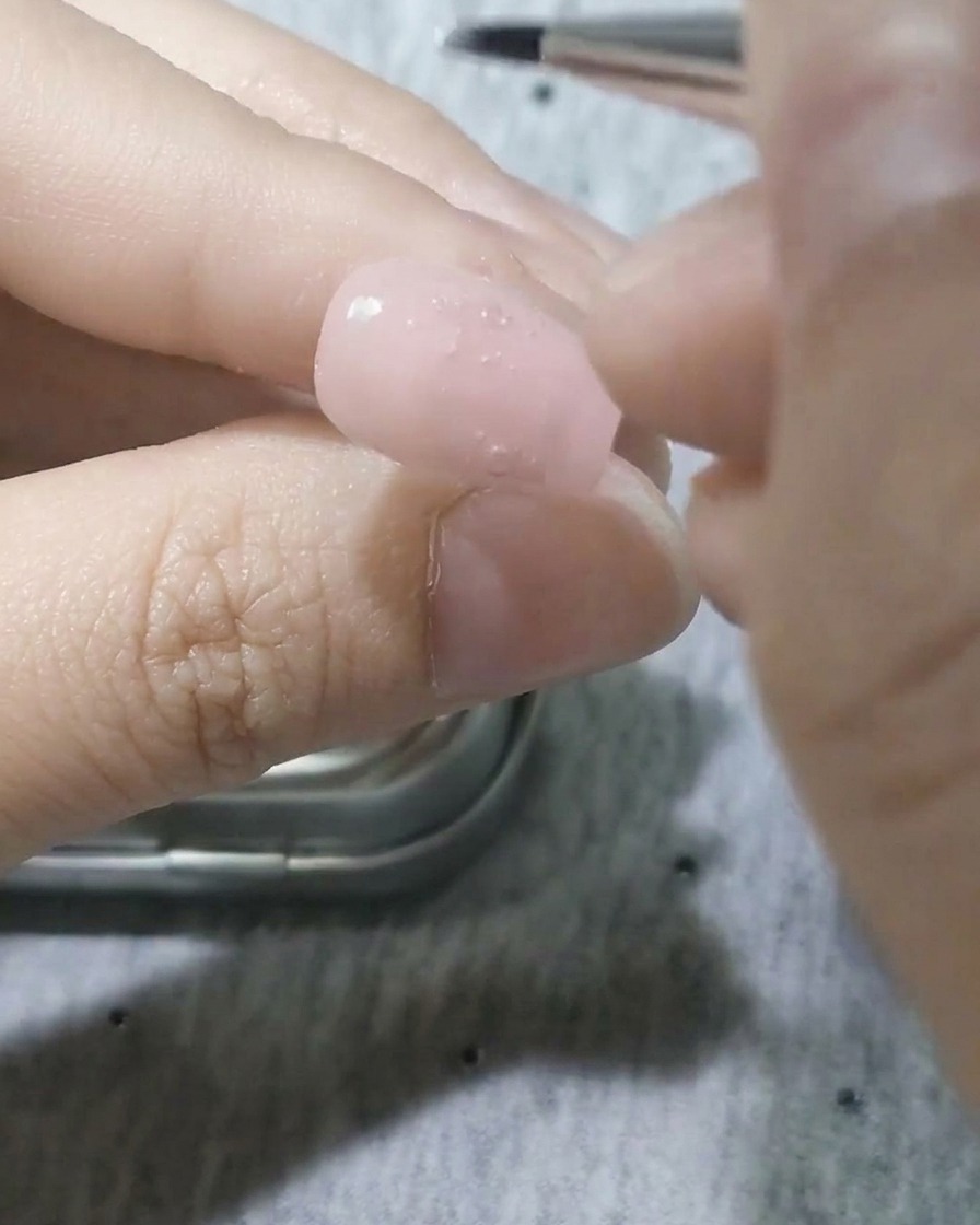 A fine detail brush applying white gel to form a petal shape on the nail.