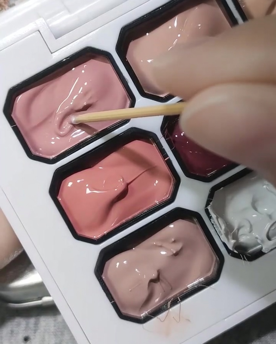 A wooden toothpick dipping into a palette of opaque cherry blossom pink gel.