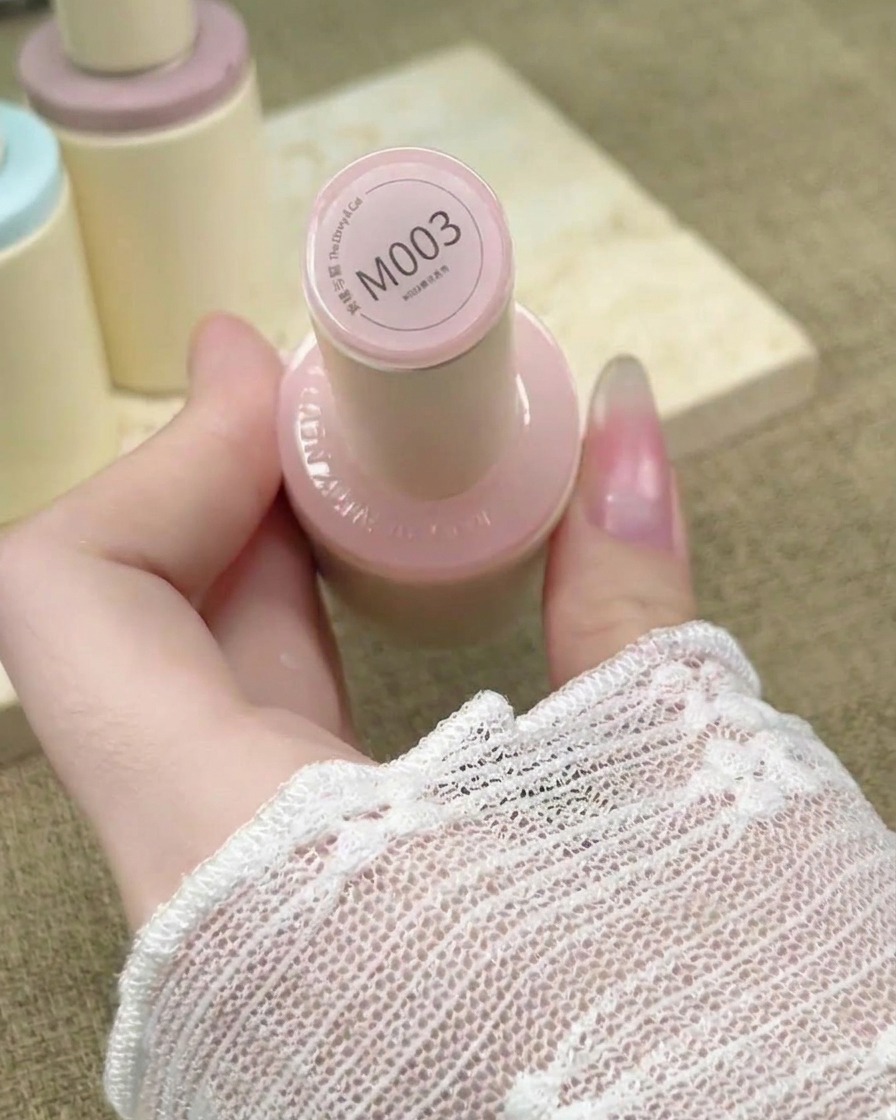 A nail brush applying a sheer nude pink gel polish over an extended nail.