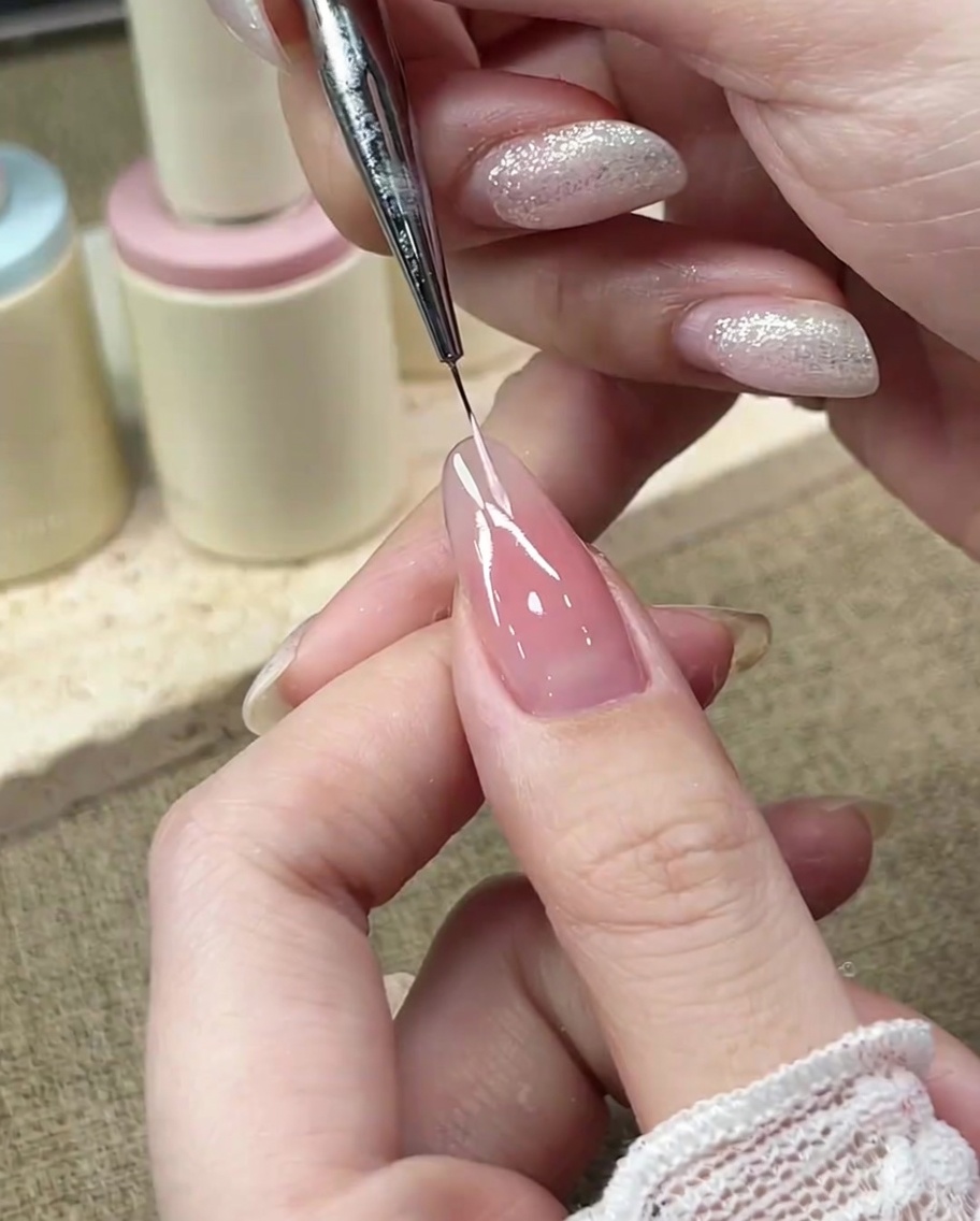 A fine detail brush drawing the left curve of a French smile line with pastel pink gel.