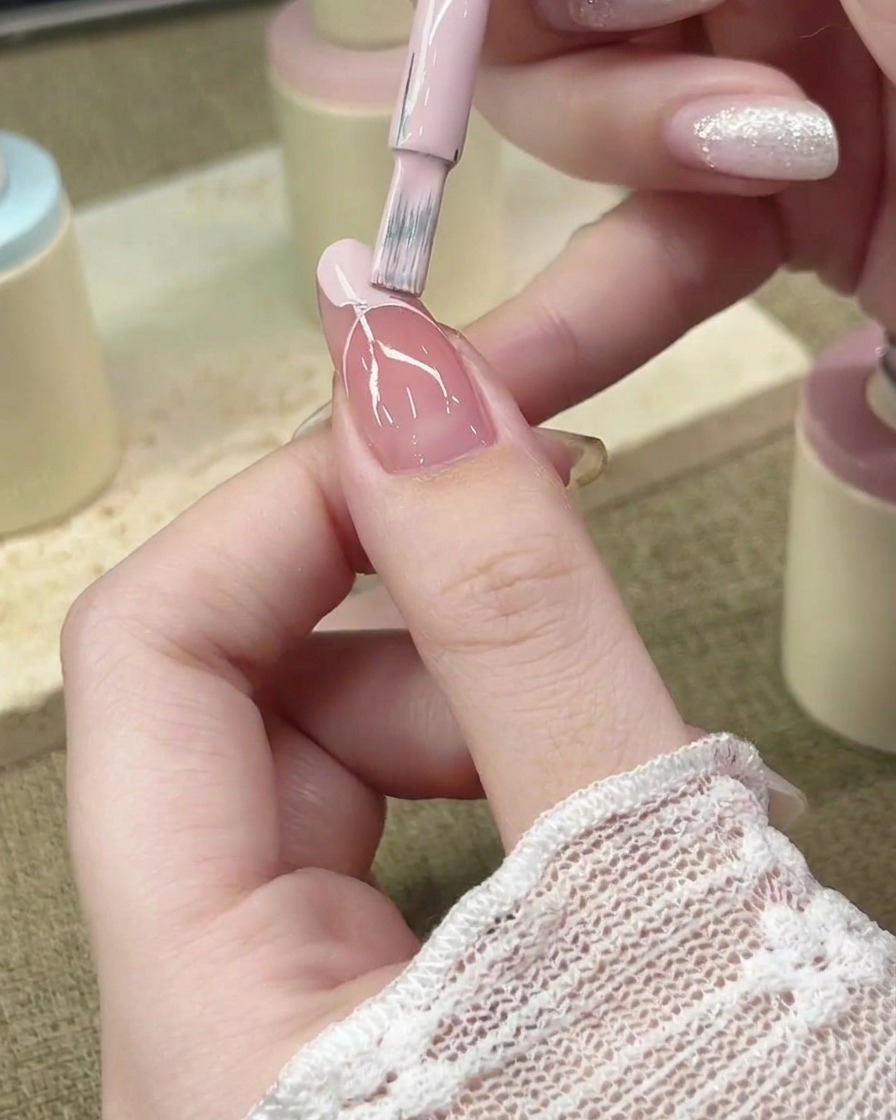 A nail brush filling in the French tip area with pastel pink gel polish.