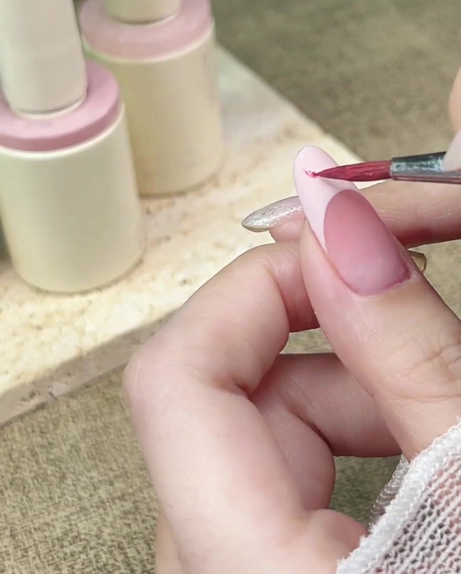 A detail brush dabbing pink watercolor onto a matte-finished French tip.