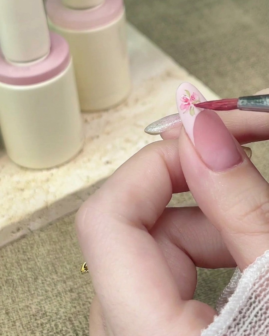 A detail brush adding more pink watercolor petals to complete a floral design on a French tip.