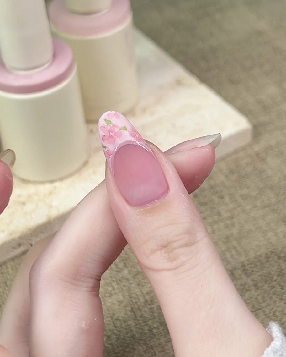 A fine liner brush adding small, thin green leaves around the pink flowers on the nail surface.