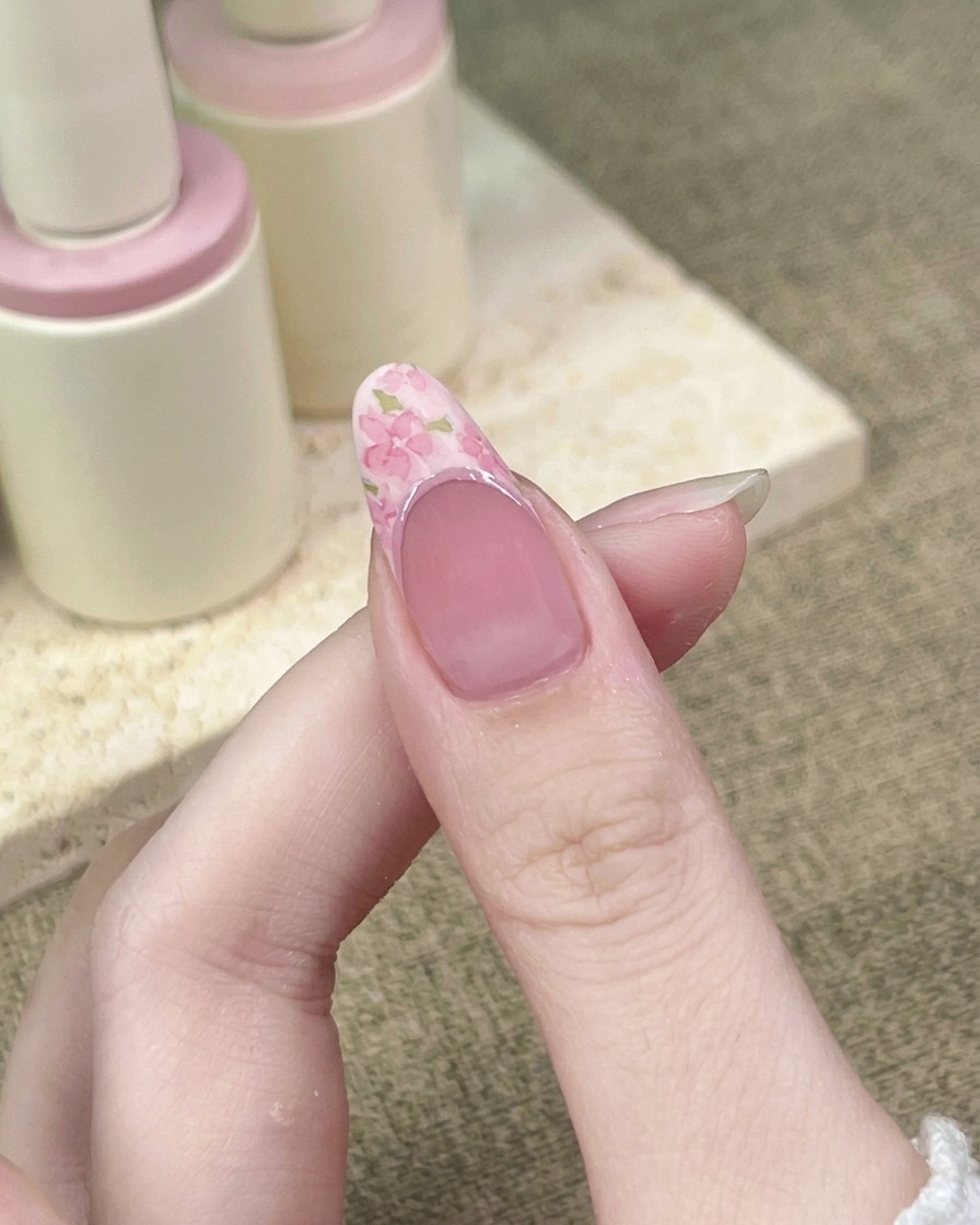 A close-up view showing a liner brush tracing a darker pink line along the curve of the French manicure smile line.