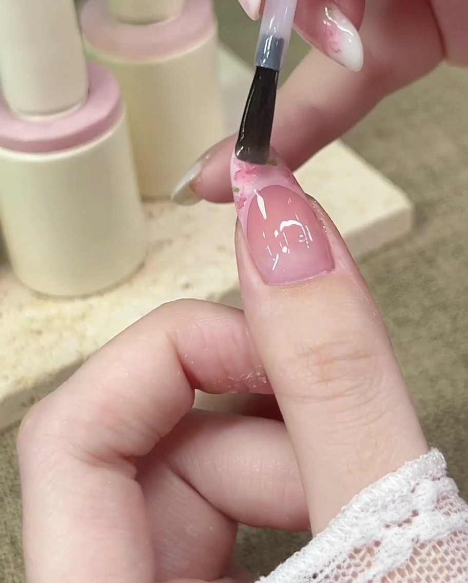A small 3D pink bow charm being placed onto the center of the French smile line using a dotting tool or tweezers.