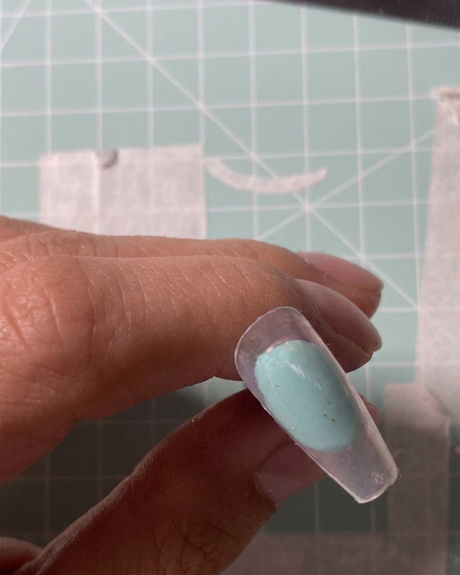 A close-up of an electric file bit buffing the surface of a clear nail tip.