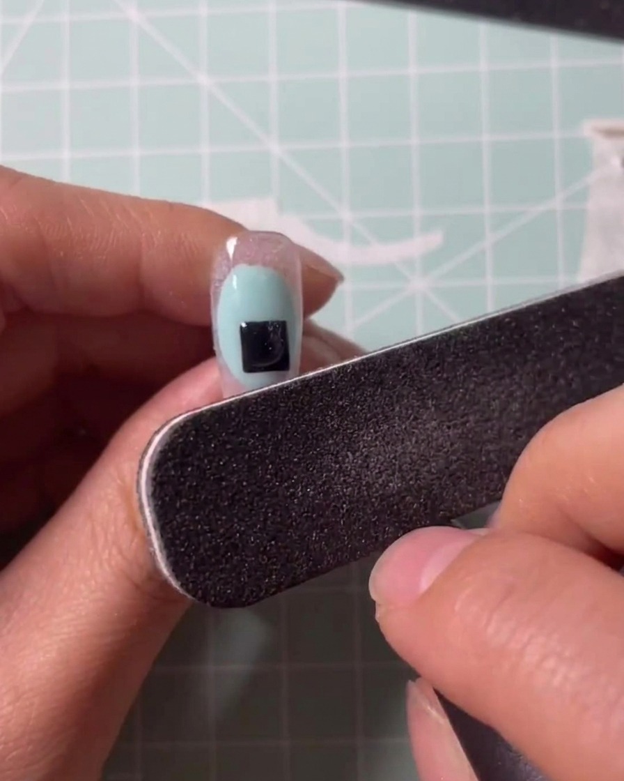 A brush applying clear gel onto a clear nail extension tip.