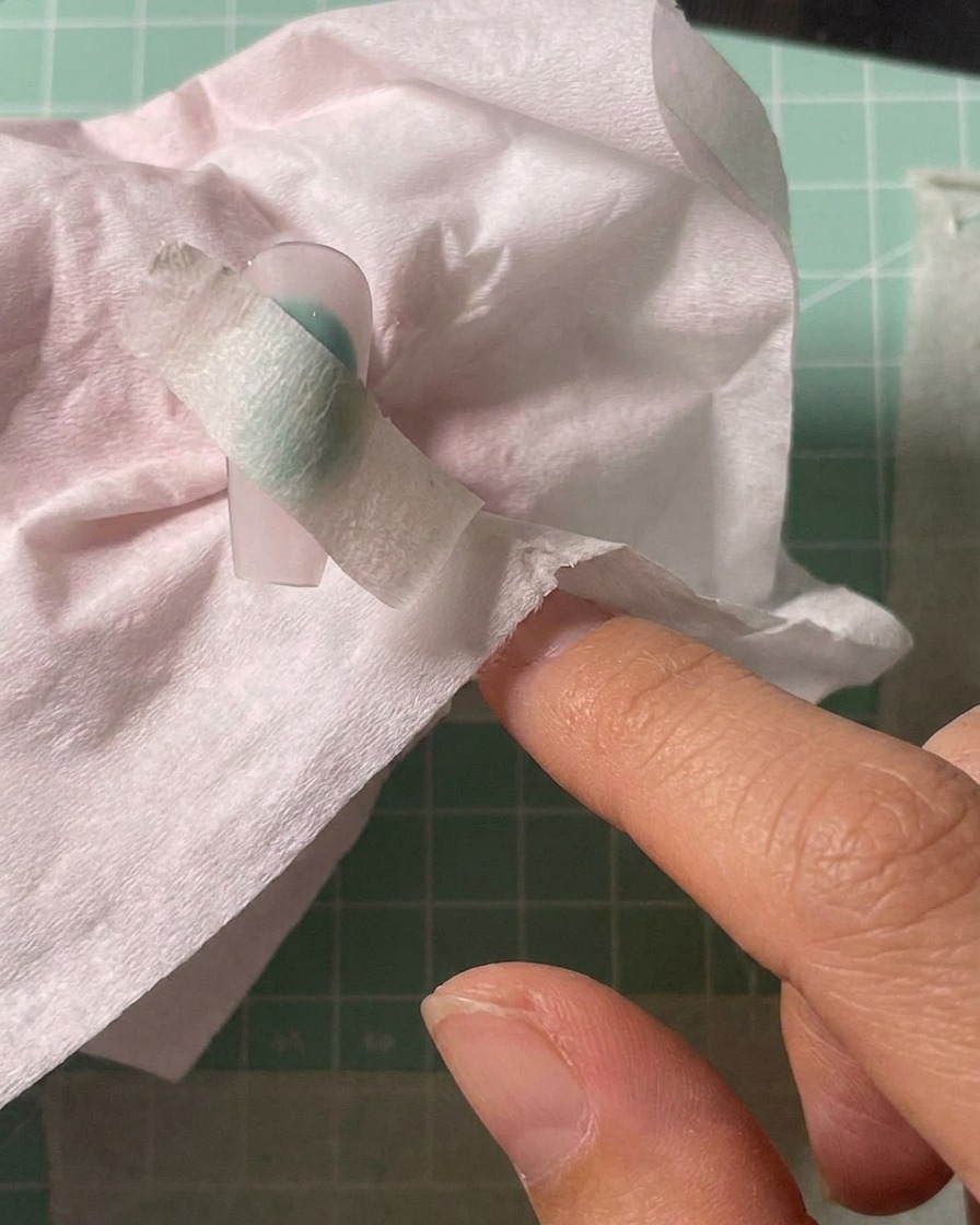 Airbrushing white pigment onto the center of a nail tip masked with a stencil.
