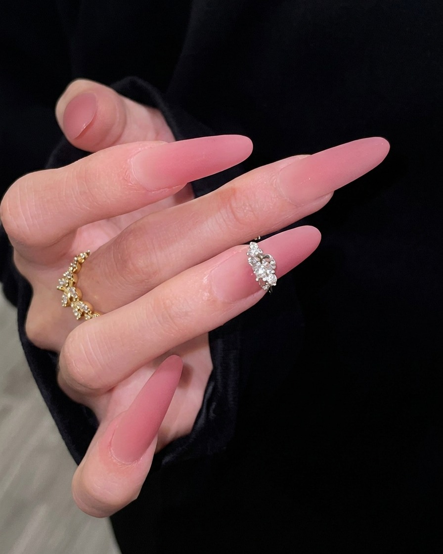 A hand with long pink gradient nails elegantly posed against a black sleeve background, highlighting the seamless transition from sheer nude to dark rose.