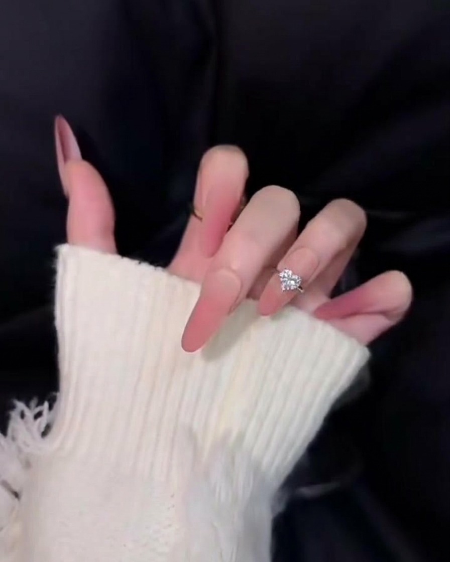A close-up of beautifully tapered long pink ombre nails against a black background, showing off a soft, diffused velvet-like finish.