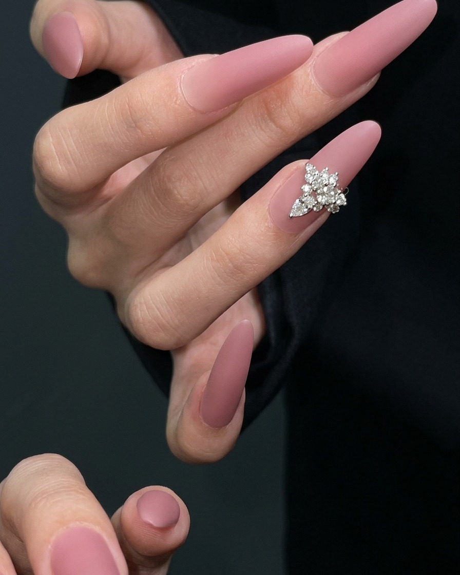 A nail art brush applying a layer of matte top coat gel onto a dried mauve-colored nail.
