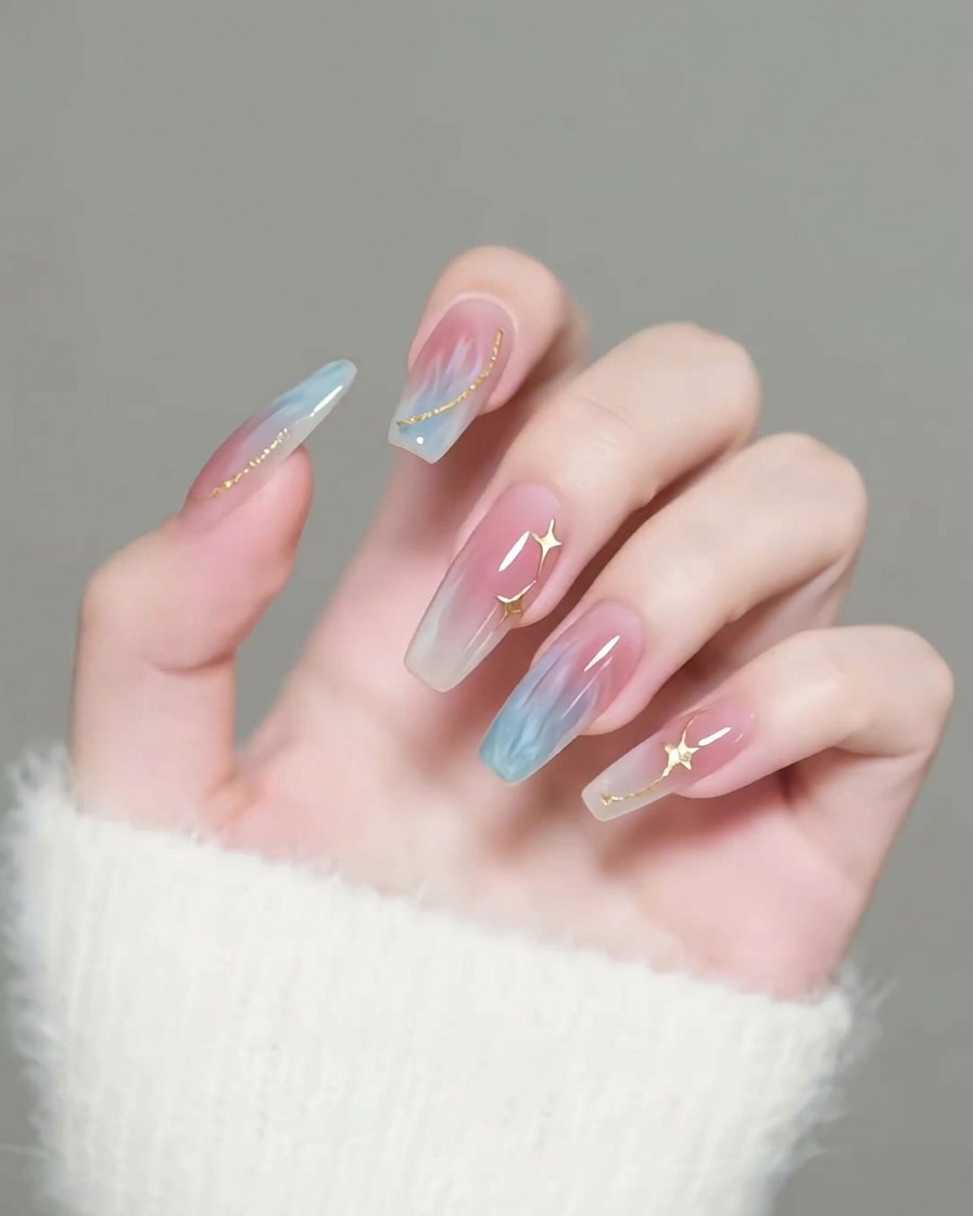 A brush applying a clear, glossy top coat over nails decorated with gold star charms.