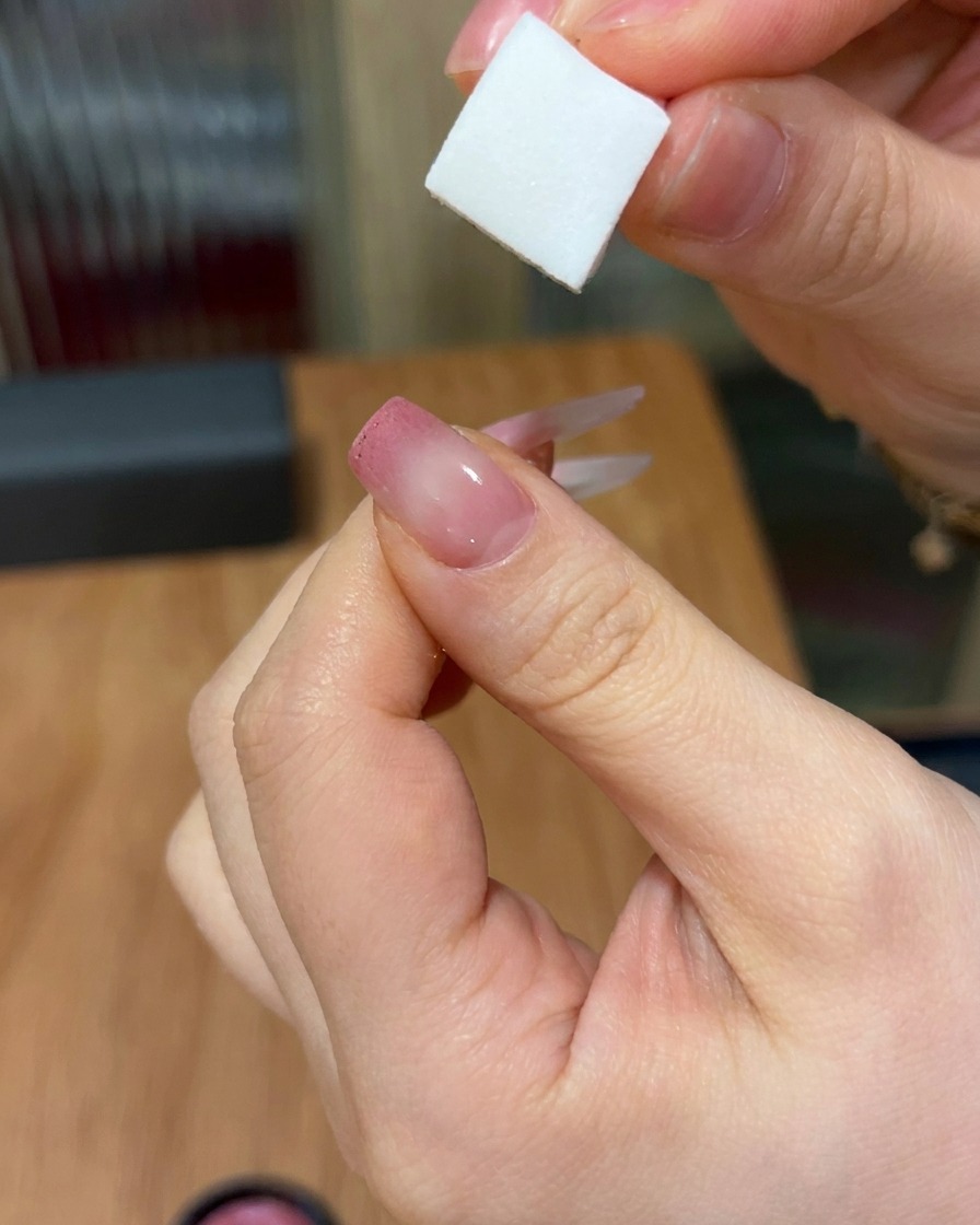 A close-up showing a sponge tapping pink gel onto a nail, creating a soft, faded gradient look from the tip toward the center.