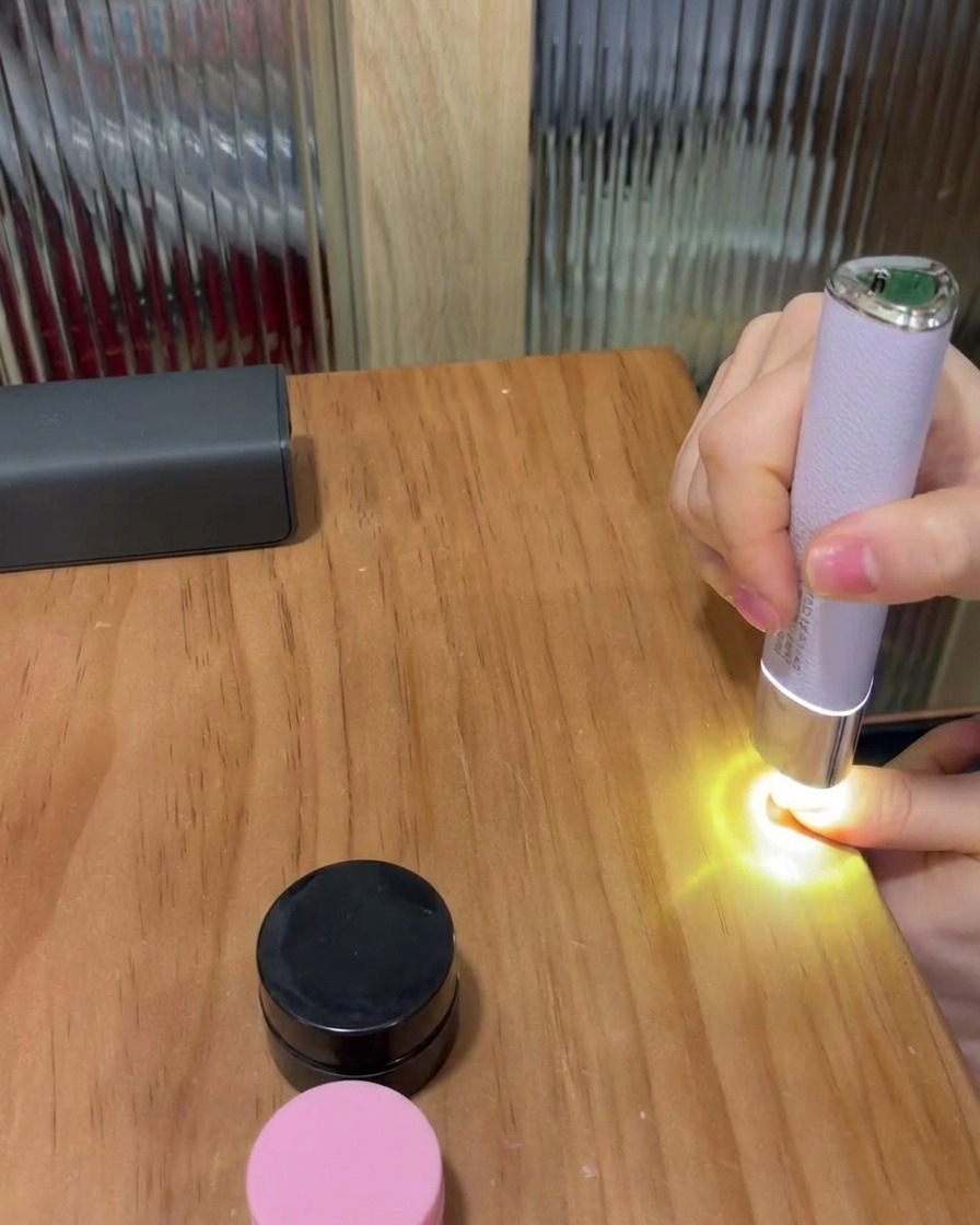 A thumbnail placed under a small, portable purple LED lamp on a wooden table, curing the gel polish.