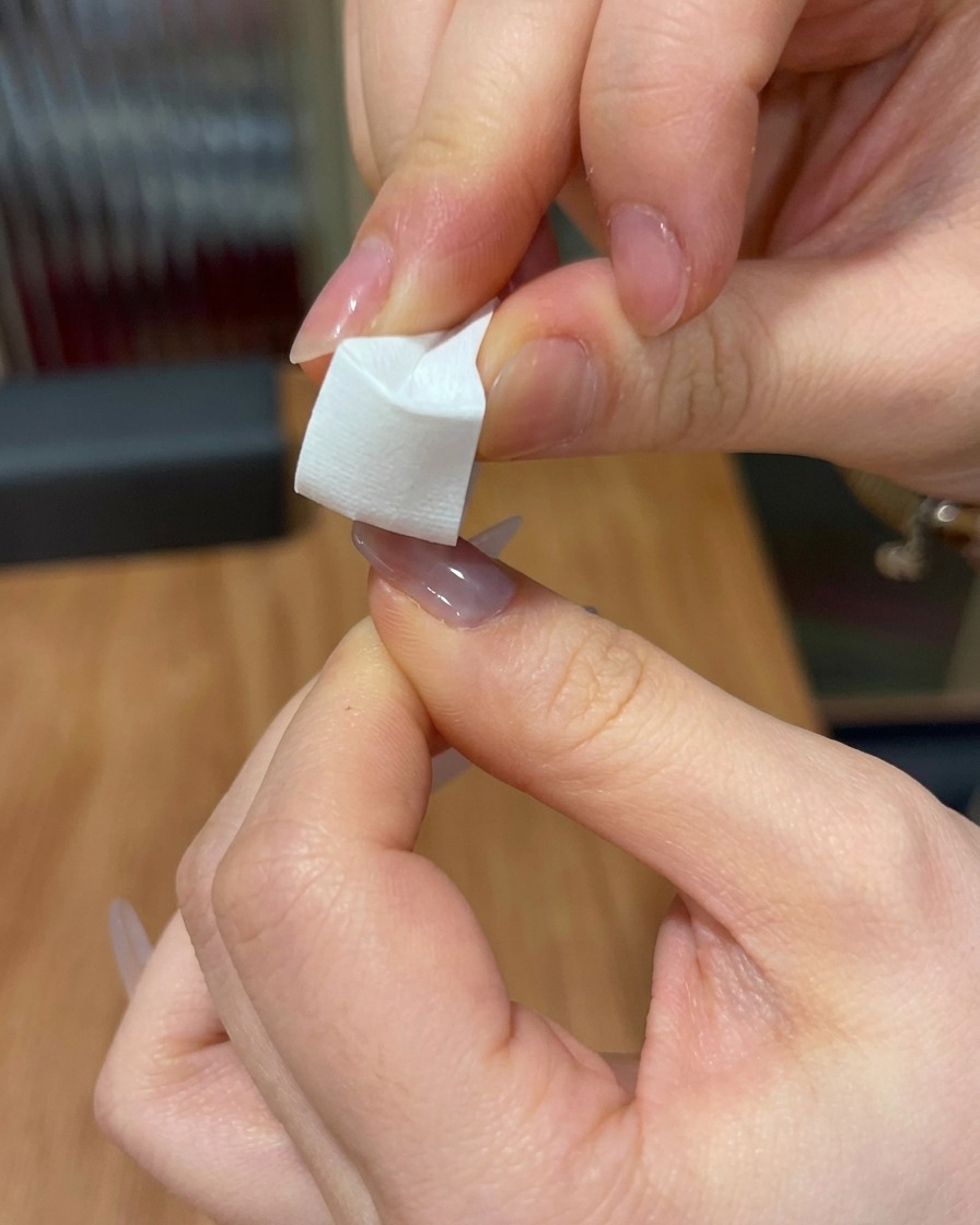A close-up of a white sponge wedge being used to pat pink gel onto the tip of a nail.