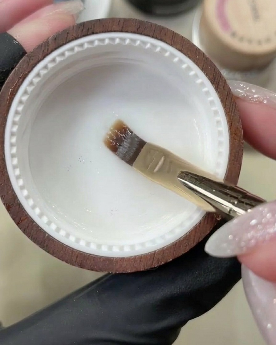 A gel brush applying a clear base coat onto a clean, natural fingernail.