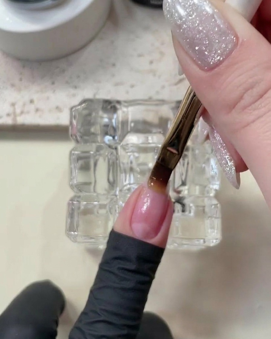 A hand placed inside a white UV/LED nail lamp, with the base coat curing on the nails.