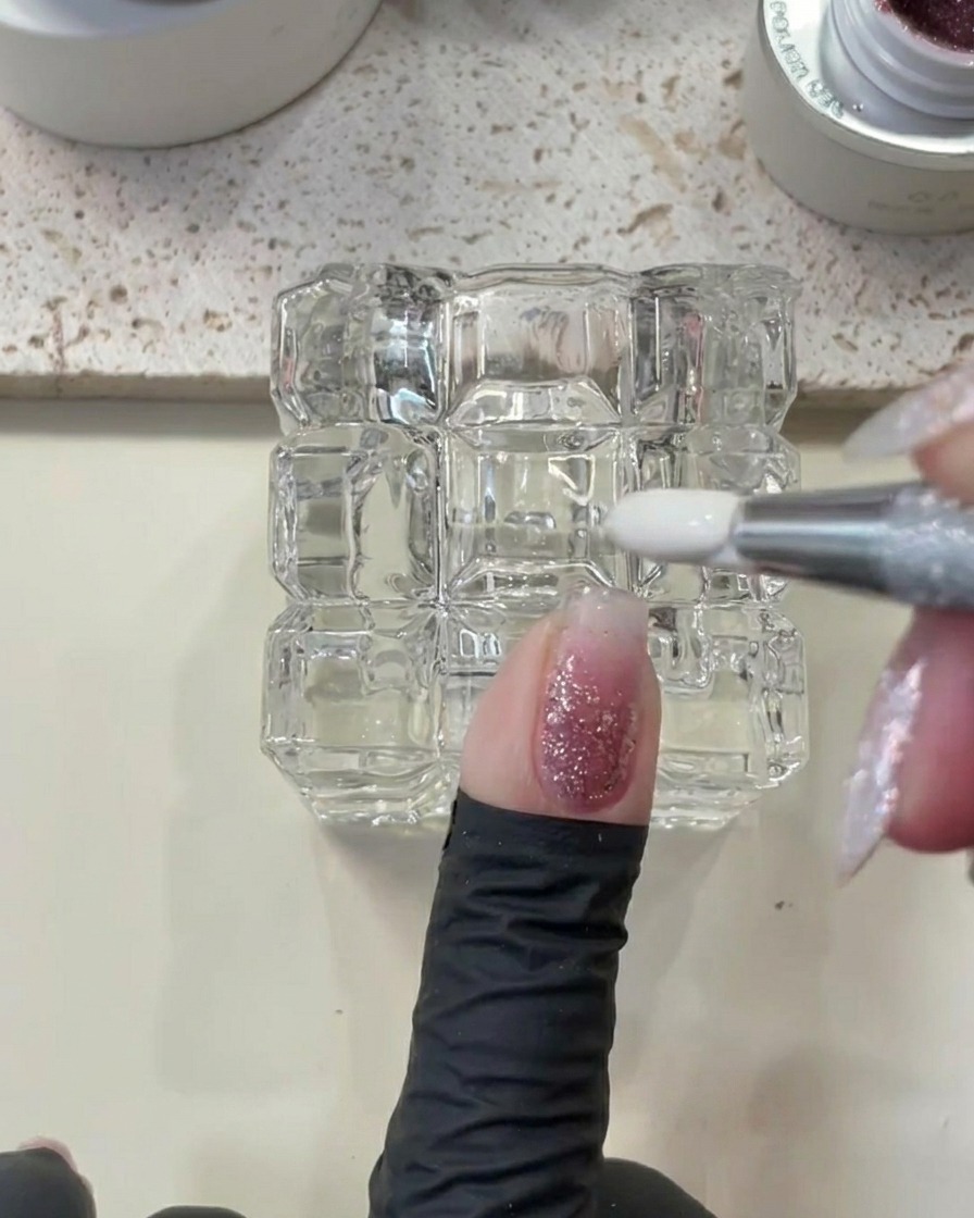 A metal tool being used to clean up excess gel around the cuticle area of a fingernail.