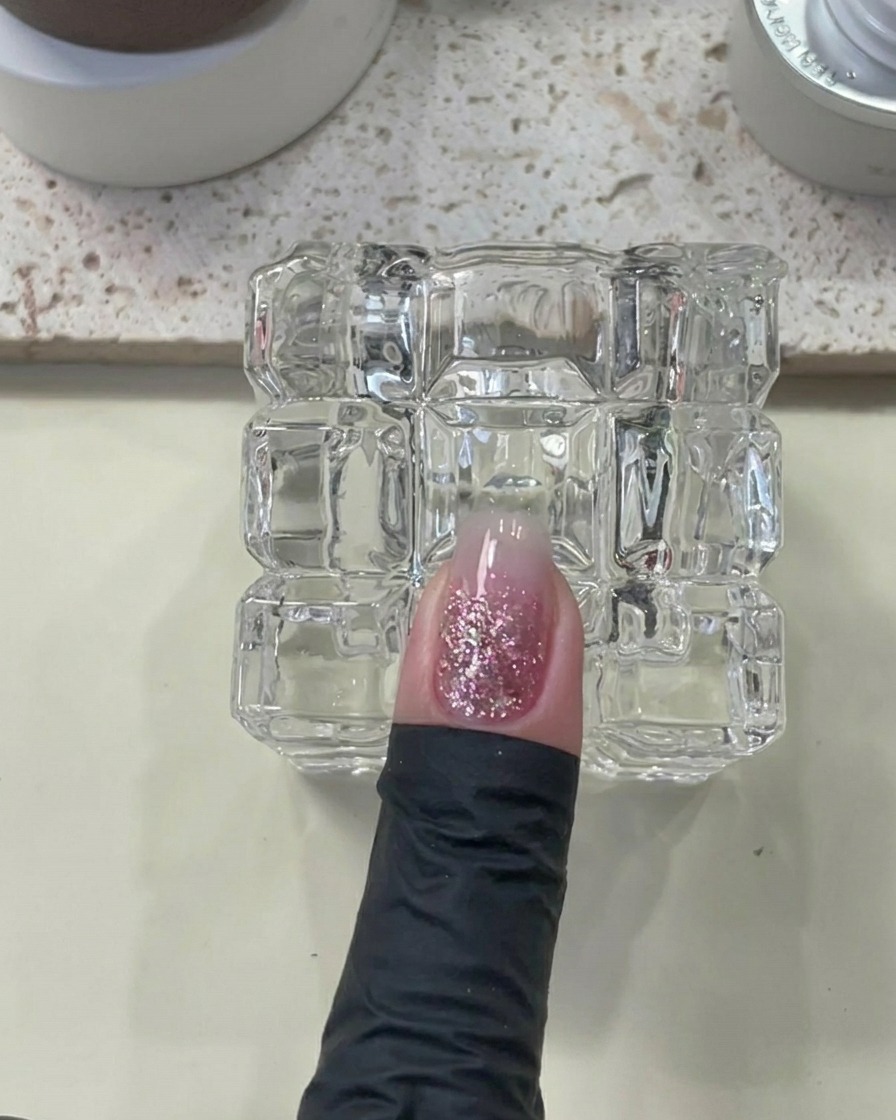 A finger with builder gel applied, placed under a UV/LED lamp.