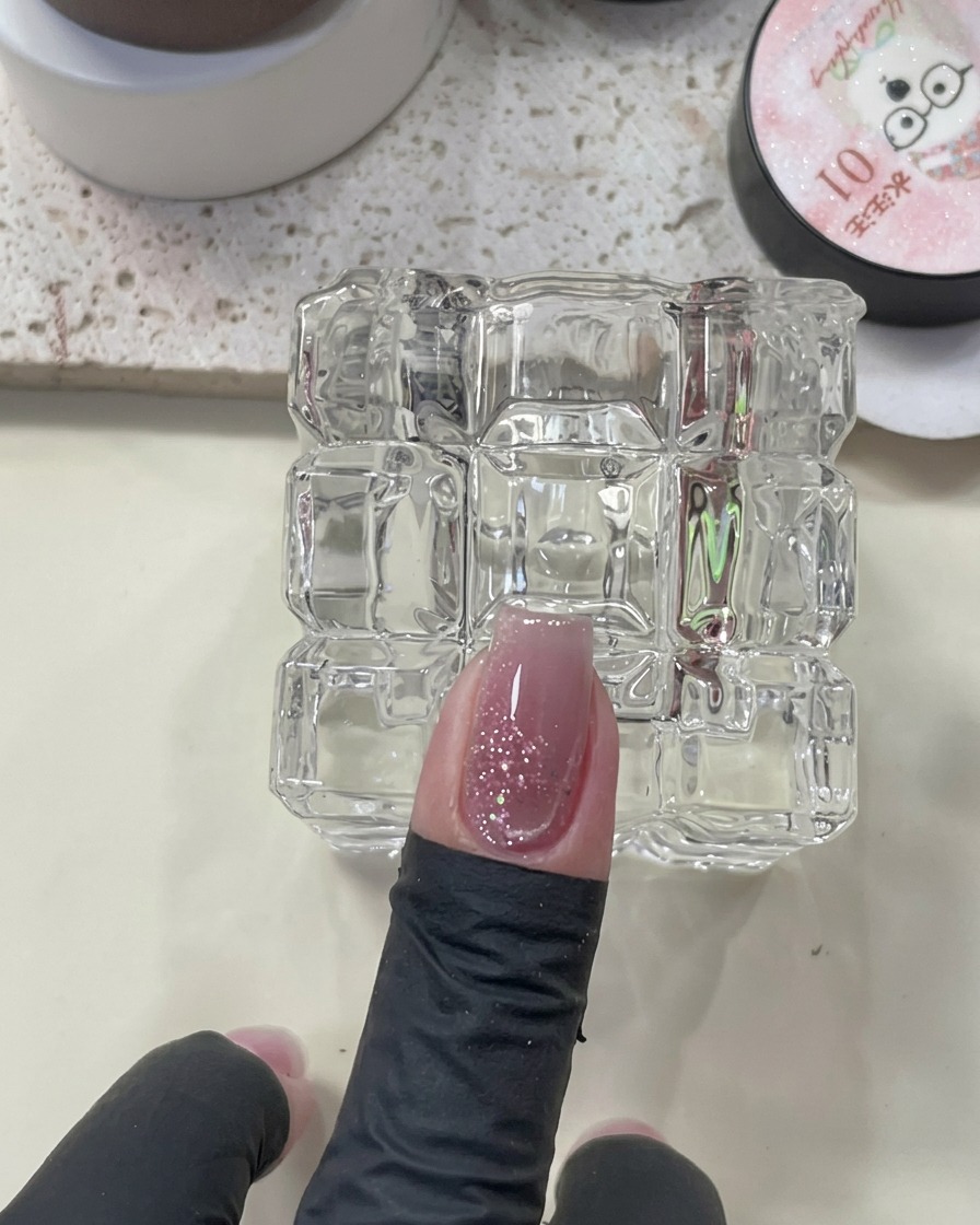 A magnetic tool positioned over a nail with wet cat-eye polish to draw out the glowing stripe.