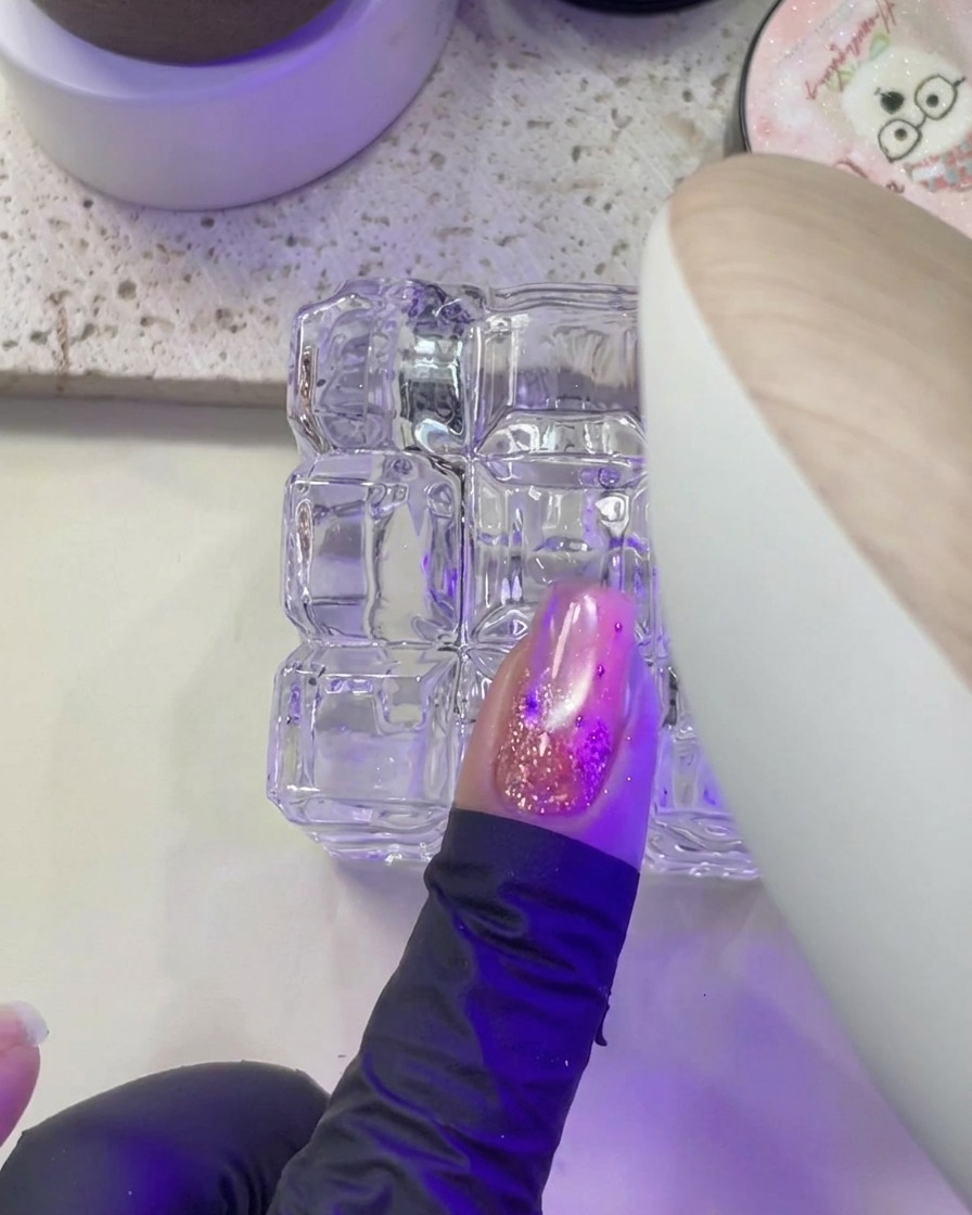 A hand placing a fingernail under the purple light of a UV/LED nail lamp for curing.