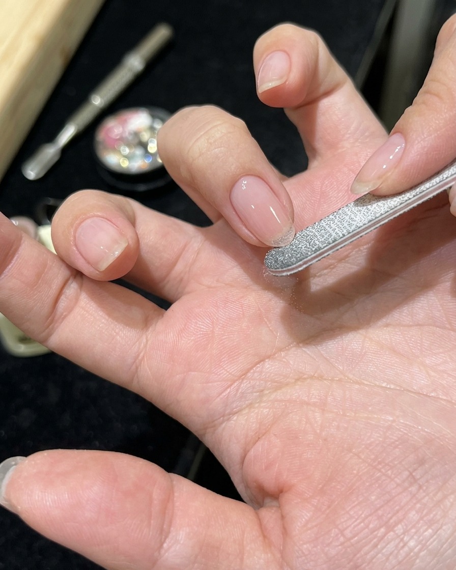 A close-up of a hand with sheer pink gel being applied to a clean natural nail.