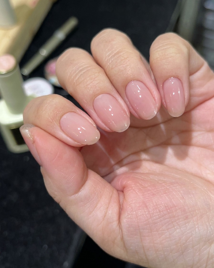 A hand positioned under a professional LED nail lamp with nails curing.