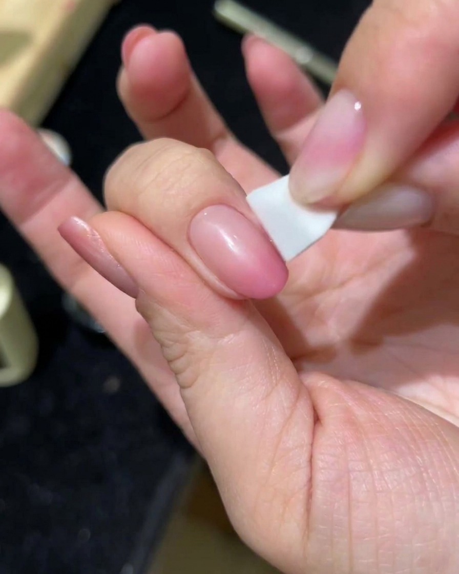 A hand dabbing a second layer of pink cat-eye gel onto a nail using a sponge.