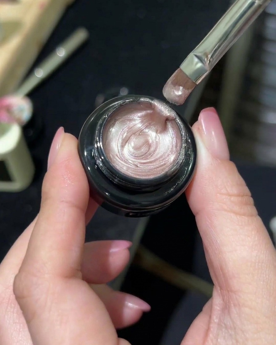 A professional nail brush picking up a shimmering, aurora-effect magnetic gel from a jar.