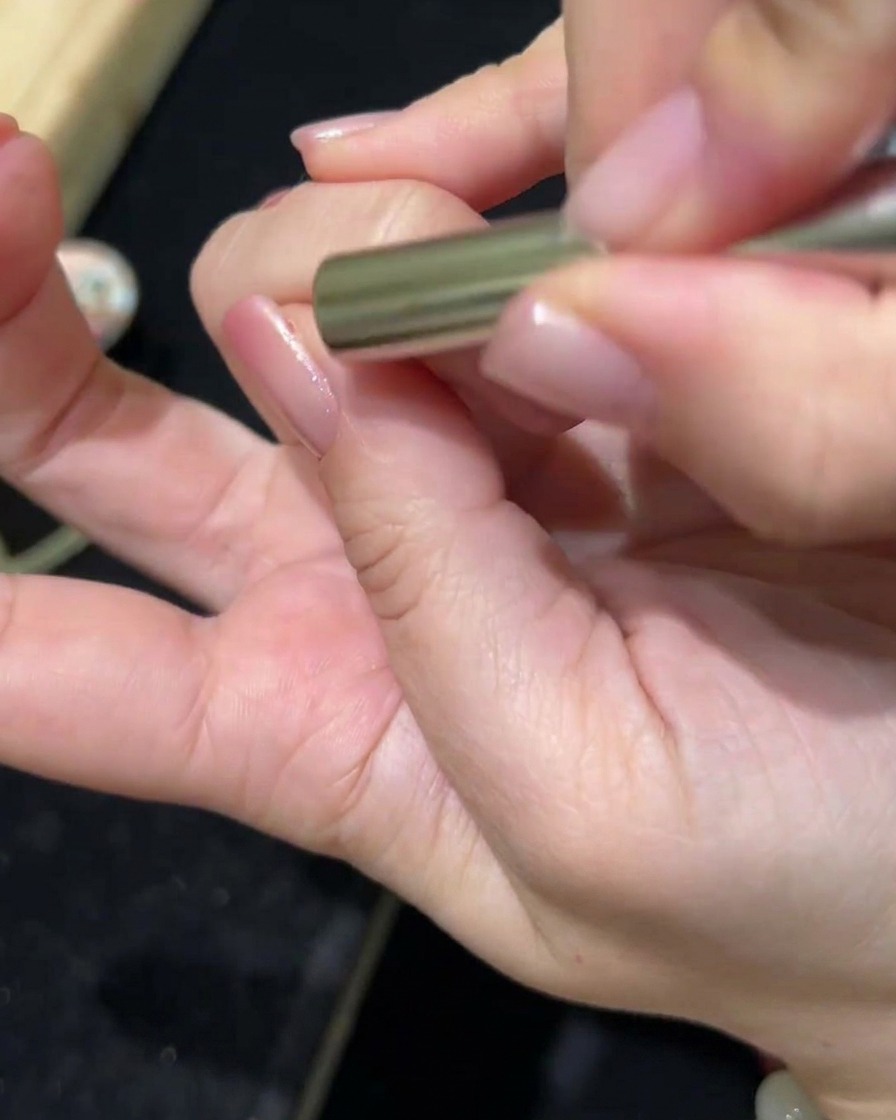 A magnetic wand being held over a nail coated with cat-eye gel, showing the pigment shifting to create a magnetic effect.