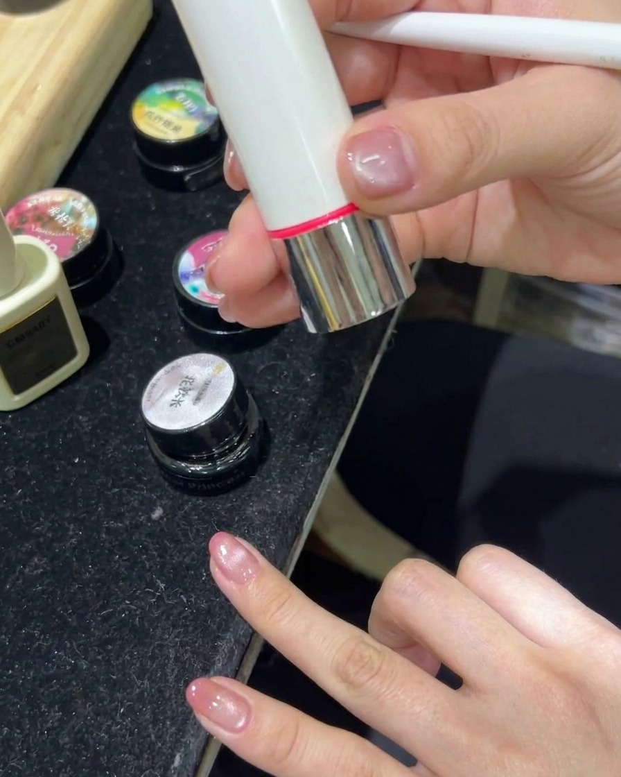 A hand resting inside an LED nail lamp with the light turned on, curing the cat-eye gel nails.