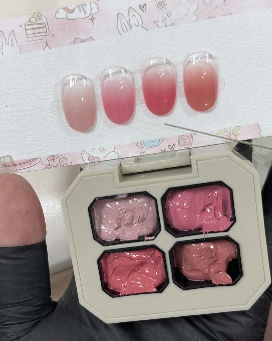 A small amount of creamy pink gel scooped onto a white surface next to the main palette.