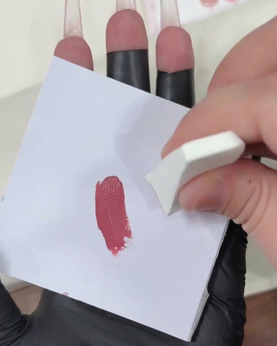 Patting a gel-loaded makeup sponge onto a clean white surface to diffuse the pink color.